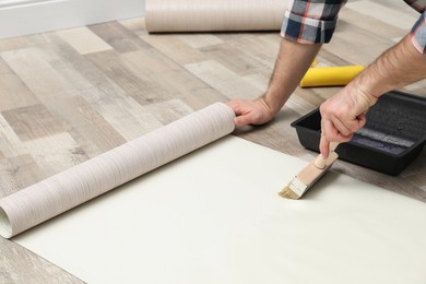 Man applying glue onto wall paper on floor, closeup