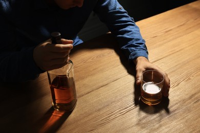 Addicted man with alcoholic drink at wooden table, closeup