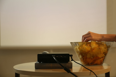 Woman eating chips while watching movie using video projector at home, closeup