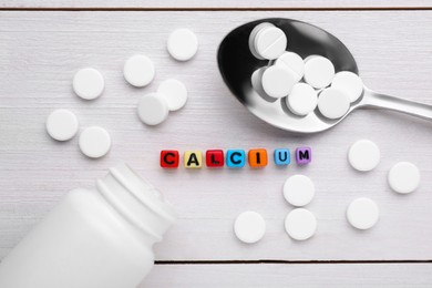 Word Calcium made of colorful plastic beads with letters, medical bottle and pills on white wooden table, flat lay