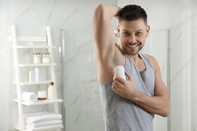 Handsome man applying deodorant in bathroom. Space for text