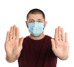 Man in protective mask showing stop gesture on white background. Prevent spreading of coronavirus