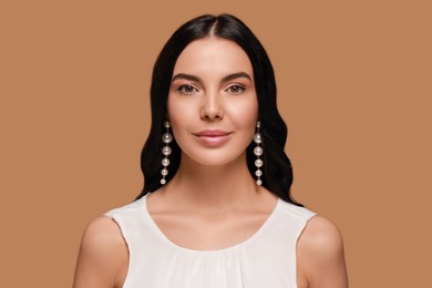 Young woman wearing elegant pearl earrings on brown background