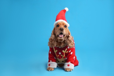 Adorable Cocker Spaniel in Christmas sweater and Santa hat on light blue background