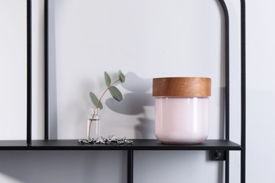 Jar of hand cream, jewelry and eucalyptus branch on shelf