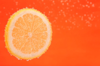Slice of lemon in sparkling water on orange background, space for text. Citrus soda