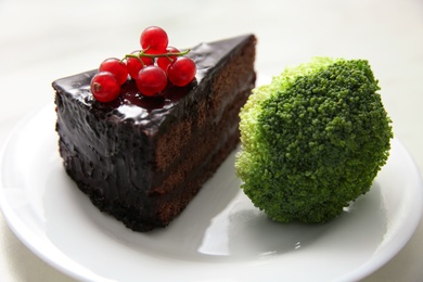 Concept of choice between healthy and junk food, closeup. Tasty cake with broccoli on plate, closeup