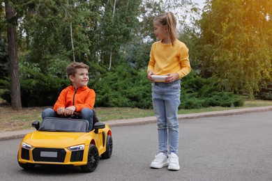 Photo of Cute girl operating children's car with little boy outdoors