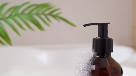 Bottle of bubble bath with foam on tub indoors, closeup. Space for text