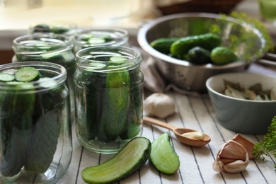 Photo of Glass jars with fresh cucumbers and other ingredients on table, closeup. Canning vegetables