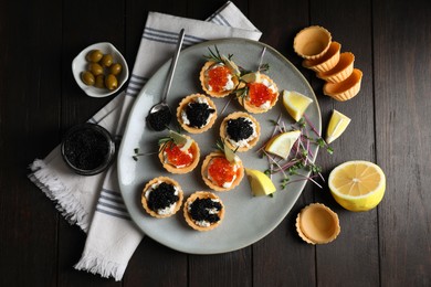 Photo of Delicious tartlets with red and black caviar served on wooden table, flat lay