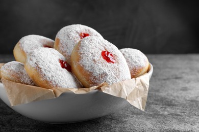 Delicious donuts with jelly and powdered sugar in bowl on grey table