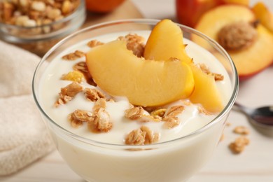 Tasty peach yogurt with granola and pieces of fruit in dessert bowl on table, closeup