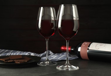Glasses and bottle of red wine with chocolate on grey table