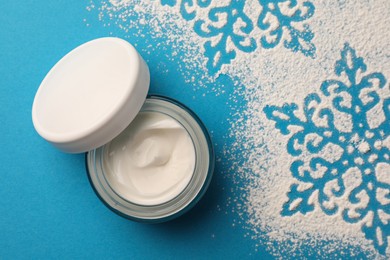 Photo of Jar of hand cream and snowflakes on light blue background, top view. Winter skin care