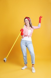 Beautiful young woman with floor brush singing on orange background
