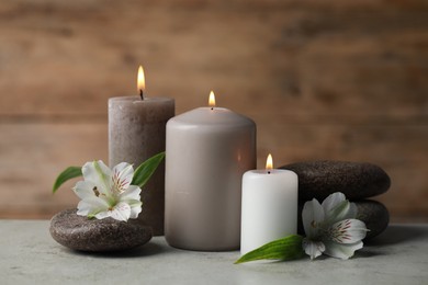 Photo of Beautiful composition with burning candles, spa stones and flowers on light grey table