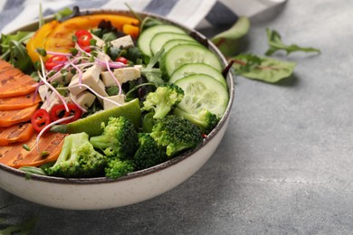Photo of Bowl with many different vegetables and tofu on grey table, closeup and space for text. Vegan diet