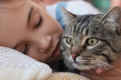 Photo of Cute little girl with her cat on bed, closeup. Childhood pet