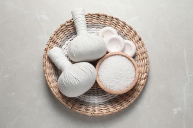 Composition with herbal massage bags and other spa products on light grey marble table, top view