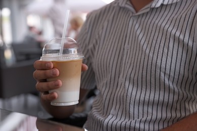 Man with plastic takeaway cup of delicious iced coffee in outdoor cafe, closeup