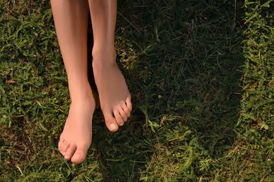 Photo of Woman sitting barefoot on green grass outdoors, top view. Space for text
