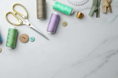 Photo of Threads and other sewing supplies on white marble table, flat lay. Space for text