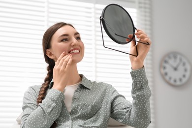 Photo of Young woman looking at her new dental implants in mirror indoors