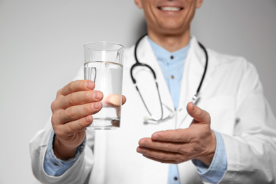 Nutritionist holding glass of pure water on light grey background, focus on hand