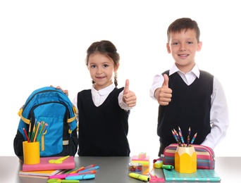 Cute children at table with school stationery on white background