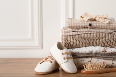 Baby clothes, shoes and hairbrush on wooden table