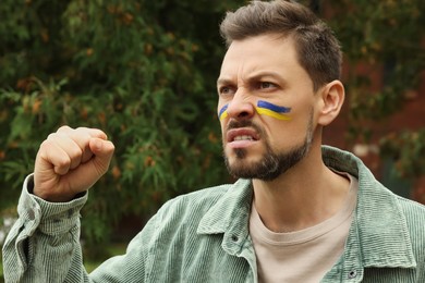 Photo of Angry man with drawings of Ukrainian flag on face outdoors