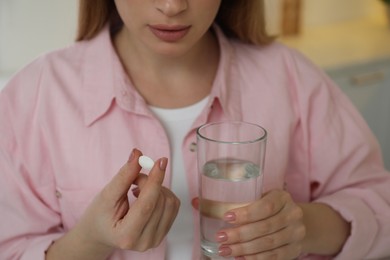 Young woman with abortion pill and water on blurred background, closeup