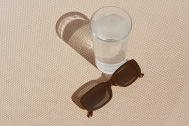 Stylish sunglasses and glass of water on grey surface, above view. Space for text