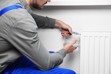 Photo of Professional plumber using pliers while preparing heating radiator for winter season, closeup