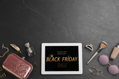 Tablet with Black Friday announcement and stylish accessories on dark table, flat lay. Space for text