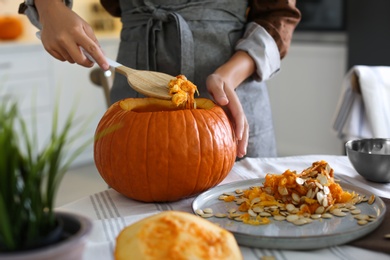 Woman making pumpkin jack o'lantern at table indoors. Halloween celebration