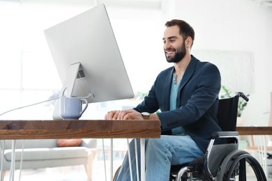 Young man in wheelchair using computer at workplace