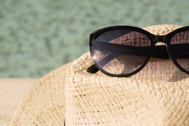Photo of Stylish hat and sunglasses near outdoor swimming pool on sunny day, closeup. Space for text