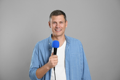 Male journalist with microphone on grey background