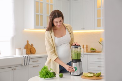 Young pregnant woman preparing smoothie at table in kitchen. Healthy eating