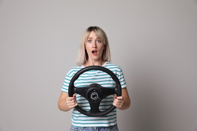 Emotional woman with steering wheel on grey background