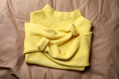 Photo of Beautiful yellow warm sweater on brown bedsheet, top view