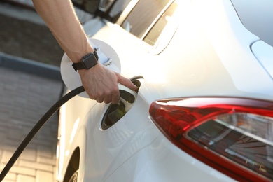 Man inserting plug into electric car socket at charging station, closeup