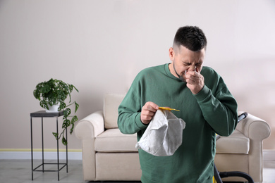 Man with vacuum cleaner bag suffering from dust allergy at home