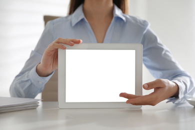 Businesswoman holding modern tablet with blank screen at white table in office, closeup