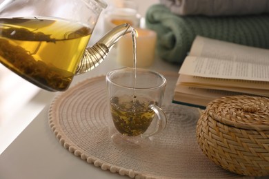 Photo of Pouring freshly brewed tea into cup at table in room, closeup. Cozy home atmosphere