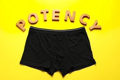 Men underwear and word Potency made of wooden letters on yellow background, flat lay