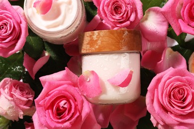Jars of face cream among beautiful roses, top view