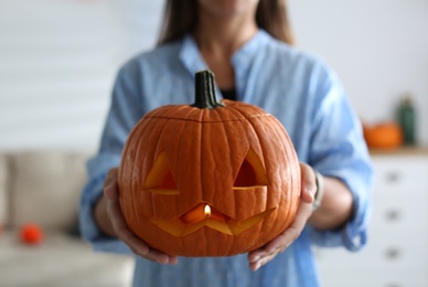 Woman holding pumpkin jack o'lantern indoors, closeup. Halloween celebration